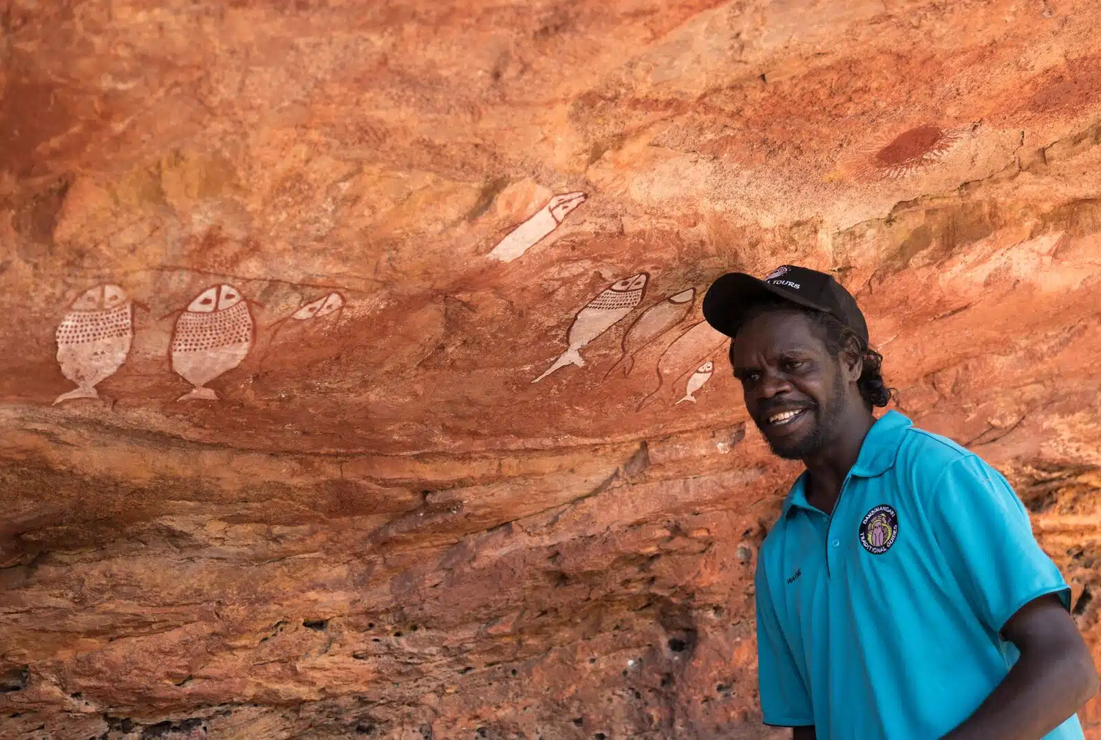 image-une Guide local aborigène en Australie devant une paroi ocre couverte de dessins rupestres