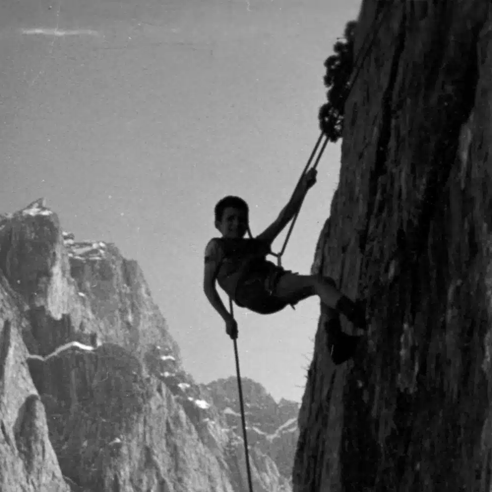 Reinhold Messner enfant accroché qui descend en rappel sur un rocher en haute montagne.