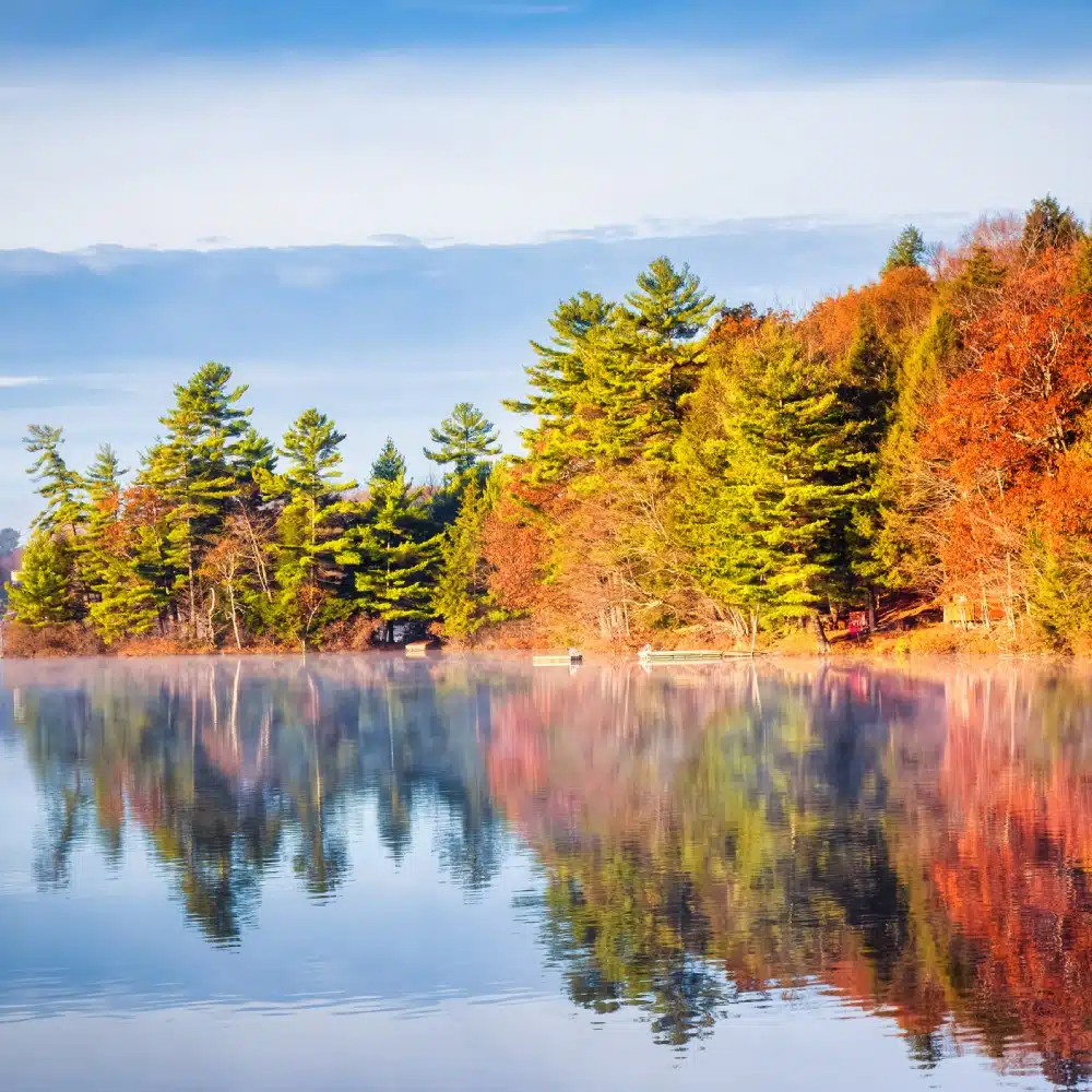 journey-canada A forest ablaze with autumn colours reflected in a lake, Canada